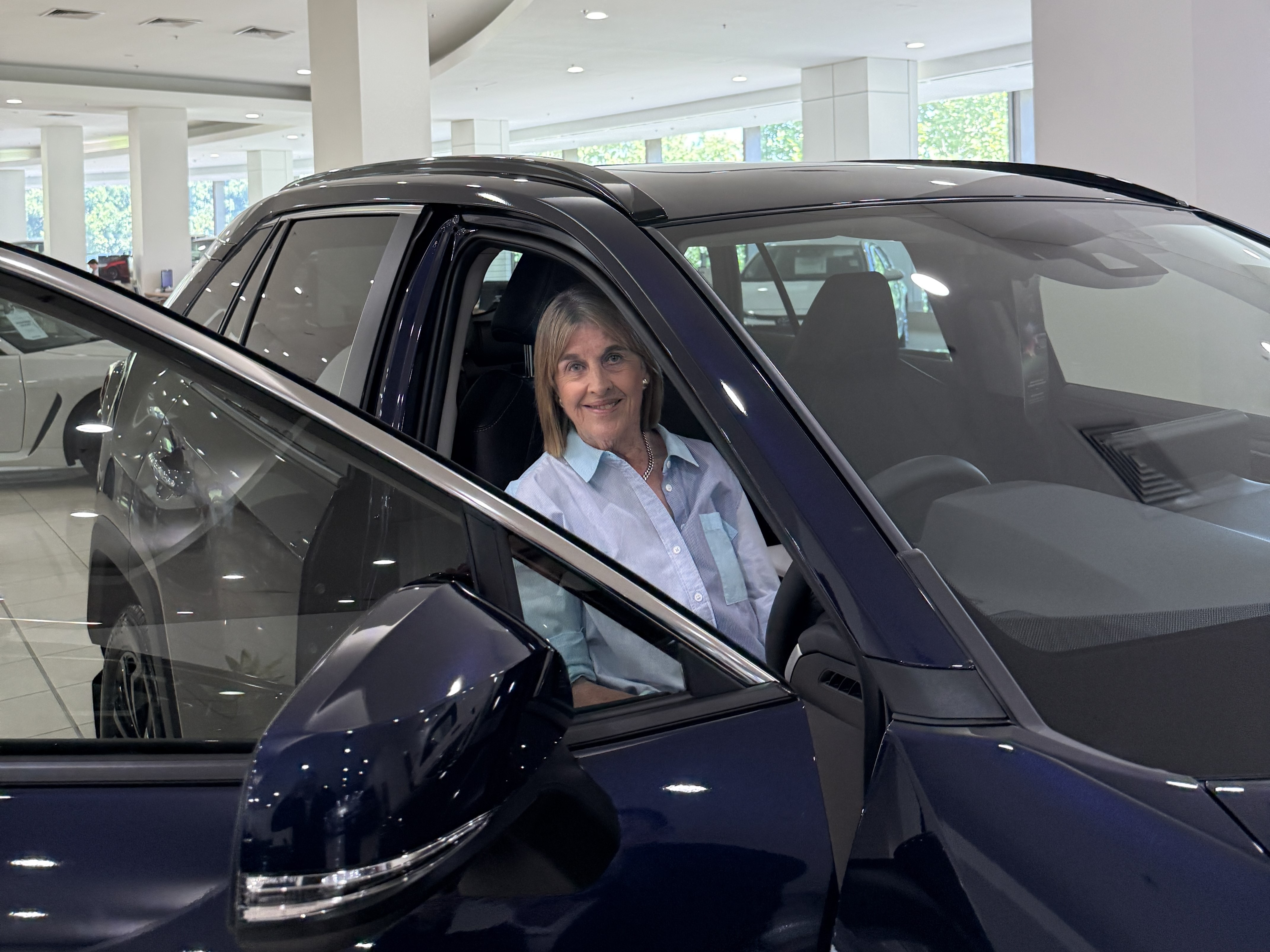 lady smiling while sitting in the driver seat of a blue Toyota RAV4 in a showroom lady smiling while sitting in the driver seat of a blue Toyota RAV4 in a showroom